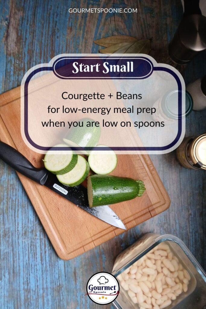 A cutting board with a chopped courgette and knife, next to a bowl of white beans on a rustic blue table. Text overlay reads: Start Small. Courgette + Beans for low-energy meal prep when you are low on spoons.
