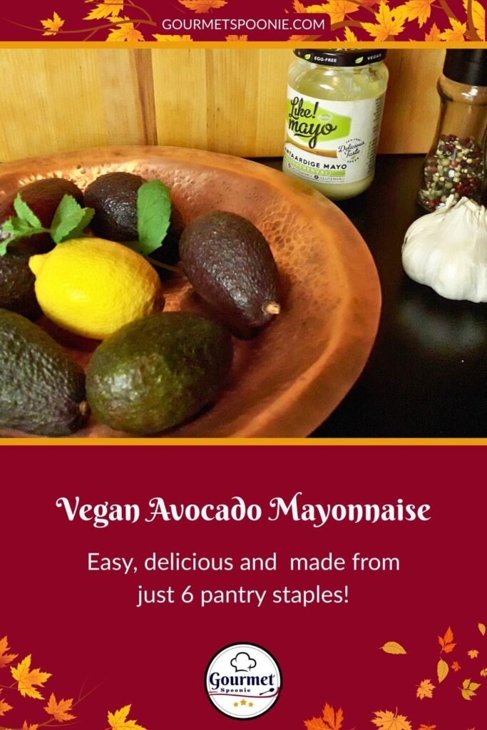 A copper bowl with fresh ingredients—avocados, a lemon, and basil—sits beside a jar of Vegan Avocado Mayonnaise, a garlic bulb, and a pepper grinder; autumn leaves frame the image with the text Vegan Avocado Mayonnaise.