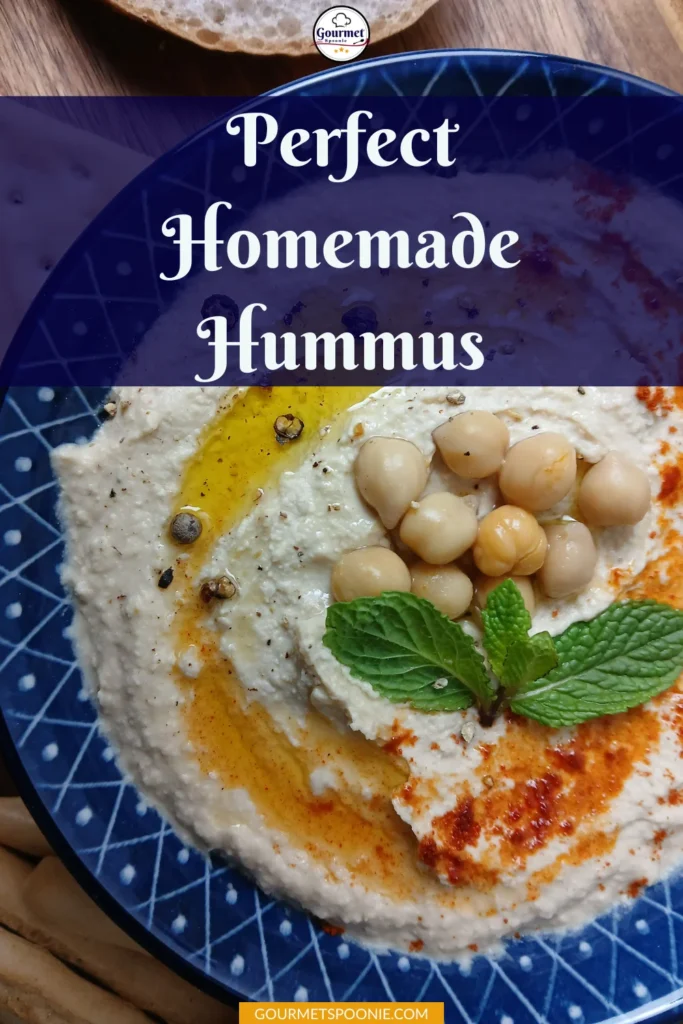 A blue plate with creamy hummus topped with whole chickpeas, olive oil, black pepper, paprika, and a mint sprig. The text Perfect Homemade Hummus appears at the top of the image.