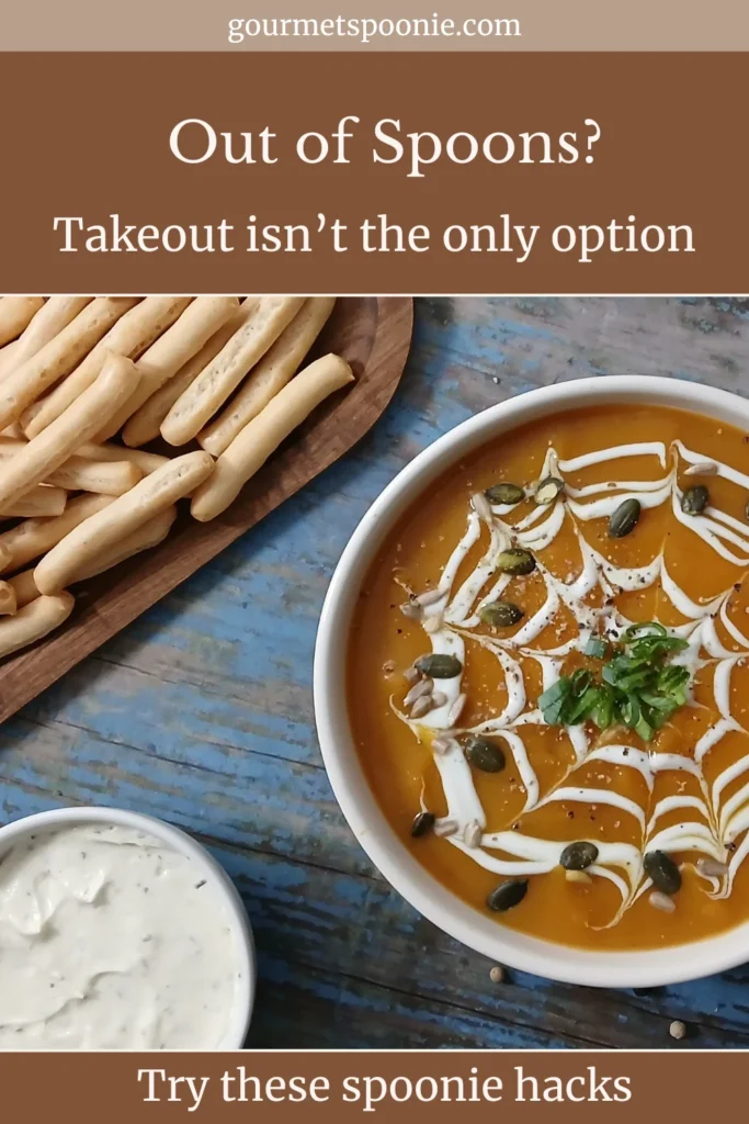 A bowl of soup with a creamy spiderweb design, a wooden dish with breadsticks, and a creamy dip sit on a blue wooden table.