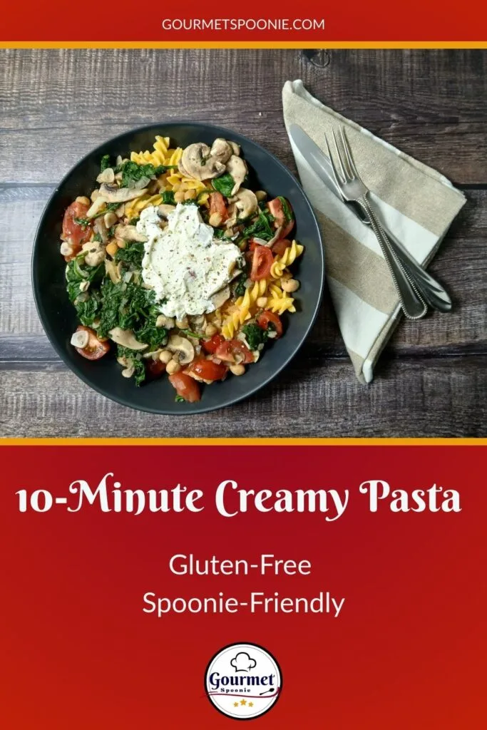 A black bowl filled with 10-Minute Creamy Pasta, mushrooms, spinach, and tomatoes sits on a wood surface next to a beige napkin with a fork and knife. Text reads: “10-Minute Creamy Pasta, Gluten-Free, Spoonie-Friendly—Gourmet Spoonie.”.