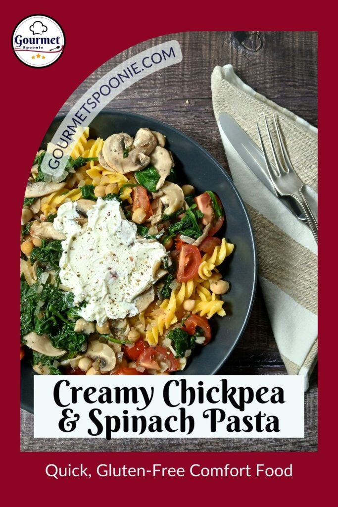 A black plate of Creamy Chickpea & Spinach Pasta topped with mushrooms and herbs, set on a wooden table with napkin, fork, and knife. Text reads, “Creamy Chickpea & Spinach Pasta. Quick, Gluten-Free Comfort Food.”.