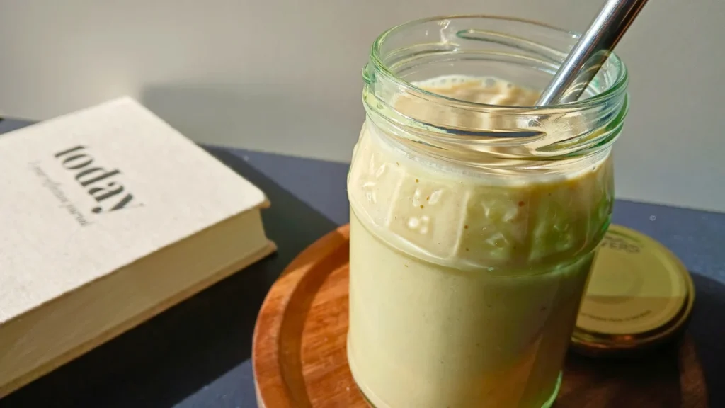 A glass jar filled with a creamy Healthy Breakfast Smoothie and a metal straw sits on a wooden coaster next to a closed diary labelled today.