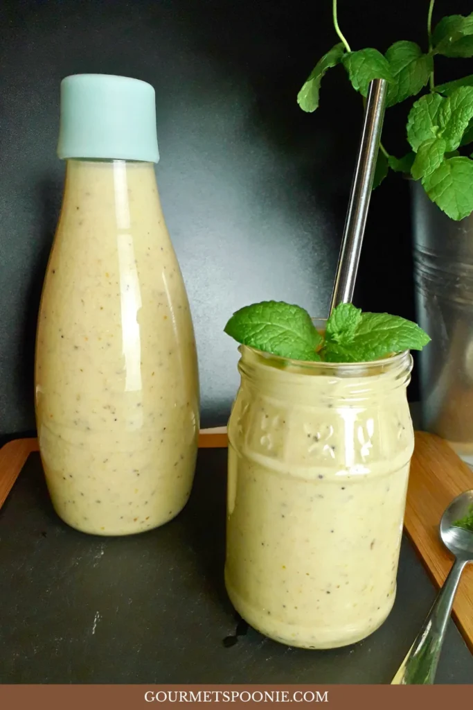 A glass bottle and a jar filled with a creamy, healthy breakfast smoothie; the jar has a metal straw and mint garnish. A pot with mint leaves is in the background.