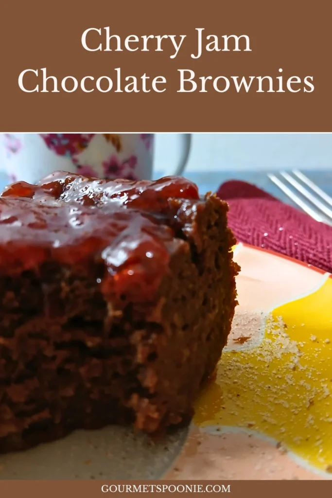 A close-up of cherry jam brownies topped with cherry sauce sits on a plate, with a floral mug in the background.