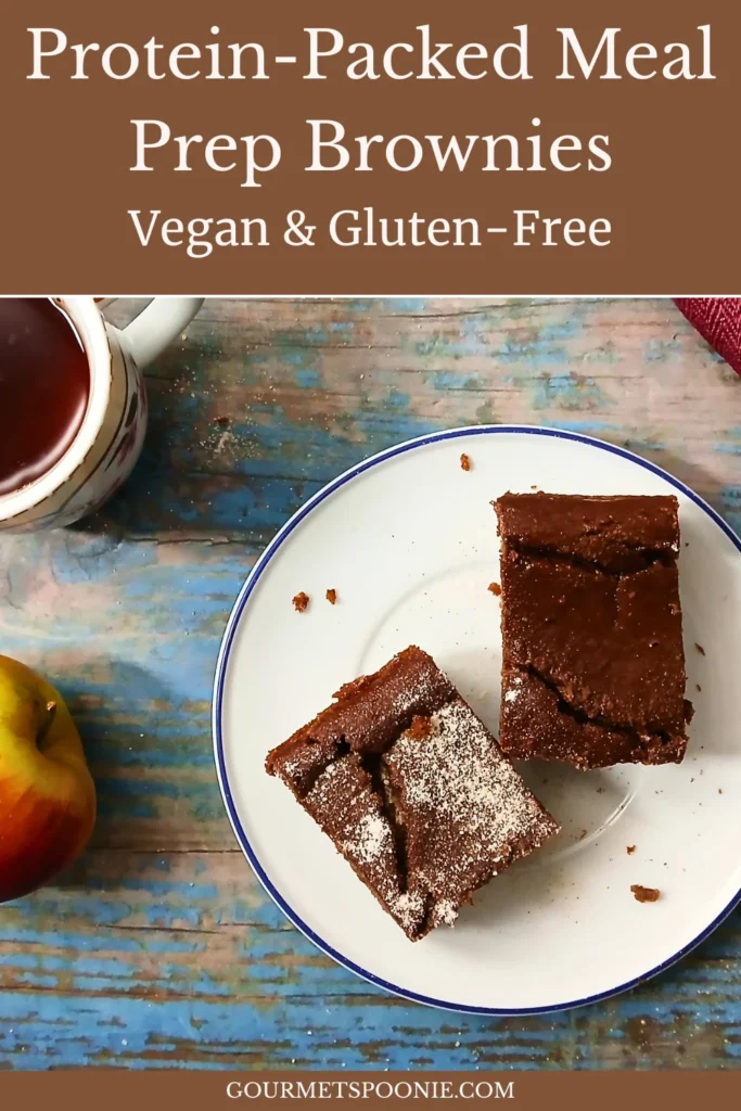 A plate with two brownies sits on a blue wooden surface next to a cup of coffee and an apple. Text at the top reads Protein-Packed Meal Prep Brownies, Vegan & Gluten-Free.