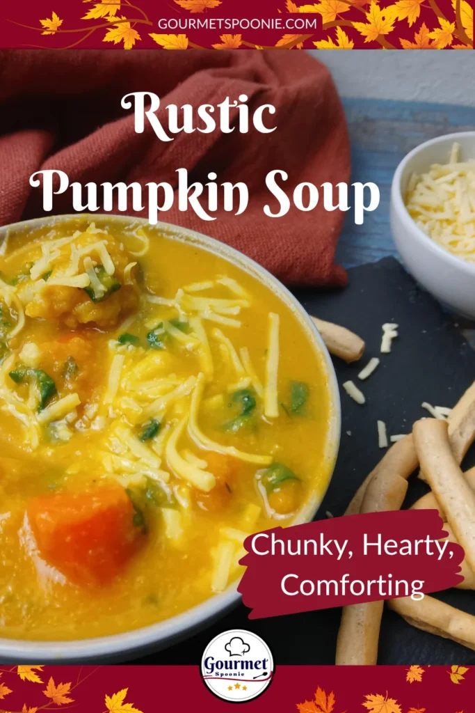 A bowl of creamy yellow warming autumn soup topped with shredded cheese sits beside a spoon and several breadsticks, with a small bowl of cheese and spice jars in the background on a rustic blue wooden surface. Text overlay reads: Rustic Pumpkin Soup. Chunky, hearty, comforting.