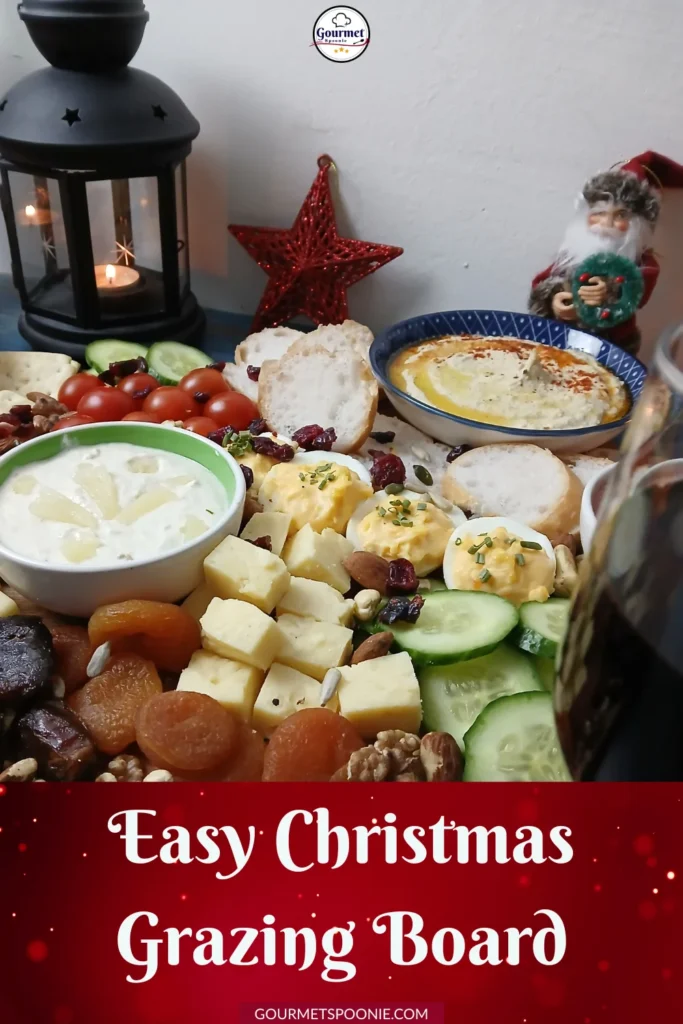A festive Christmas grazing board with cheeses, dips, nuts, fruits, crackers, fresh veggies, and holiday decorations including a lantern, red star, and Santa figurine. Text reads Easy Christmas Grazing Board.