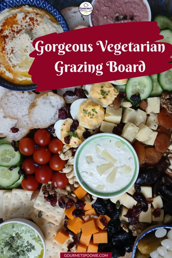 A colourful vegetarian grazing board with hummus, sliced cucumber, cherry tomatoes, cheese cubes, boiled eggs, dried fruits, nuts, crackers, and bread, artfully arranged for snacking. Text: Gorgeous Vegetarian Grazing Board.