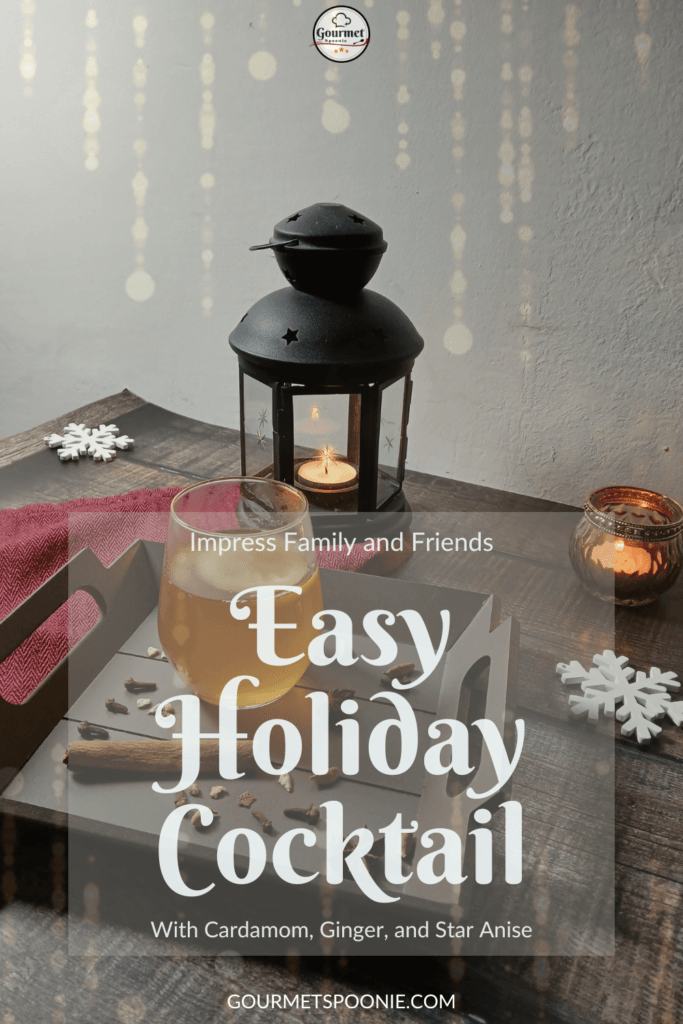 A festive holiday cocktail sits on a wooden tray next to spices, a candle-lit lantern, and decorative snowflakes. Text: Easy Holiday Cocktail with Cardamom, Ginger, and Star Anise.