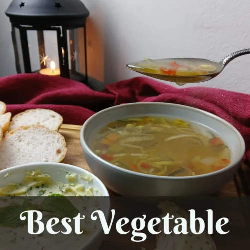 A bowl of vegetable soup with a spoonful held above it, accompanied by sliced bread and a dip, with a lit lantern and red cloth in the background. Text overlay reads: Best Vegetable Soup.
