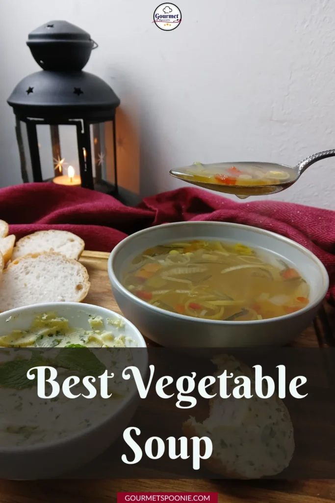 A bowl of vegetable soup with a spoonful held above it, accompanied by sliced bread and a dip, with a lit lantern and red cloth in the background. Text overlay reads: Best Vegetable Soup.