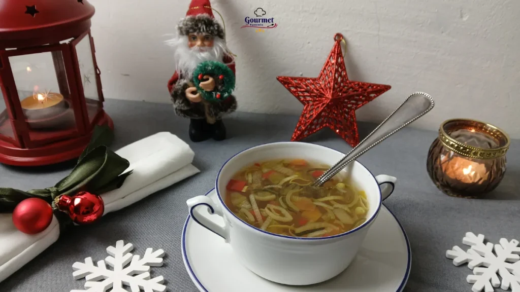 A bowl of vegetable soup with a spoon sits on a table decorated with Christmas ornaments—an inviting scene for an easy Christmas dinner, complete with a napkin with baubles, a lantern, lit candle, Santa figurine, and red star against a white wall.