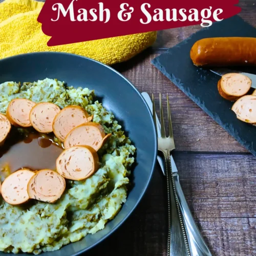 A plate of Dutch kale mash topped with sliced sausage and gravy sits next to a fork and spoon. Text reads “Dutch Kale Mash & Sausage.”.
