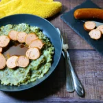 A plate of Dutch Kale Mash, topped with sliced sausage and gravy.