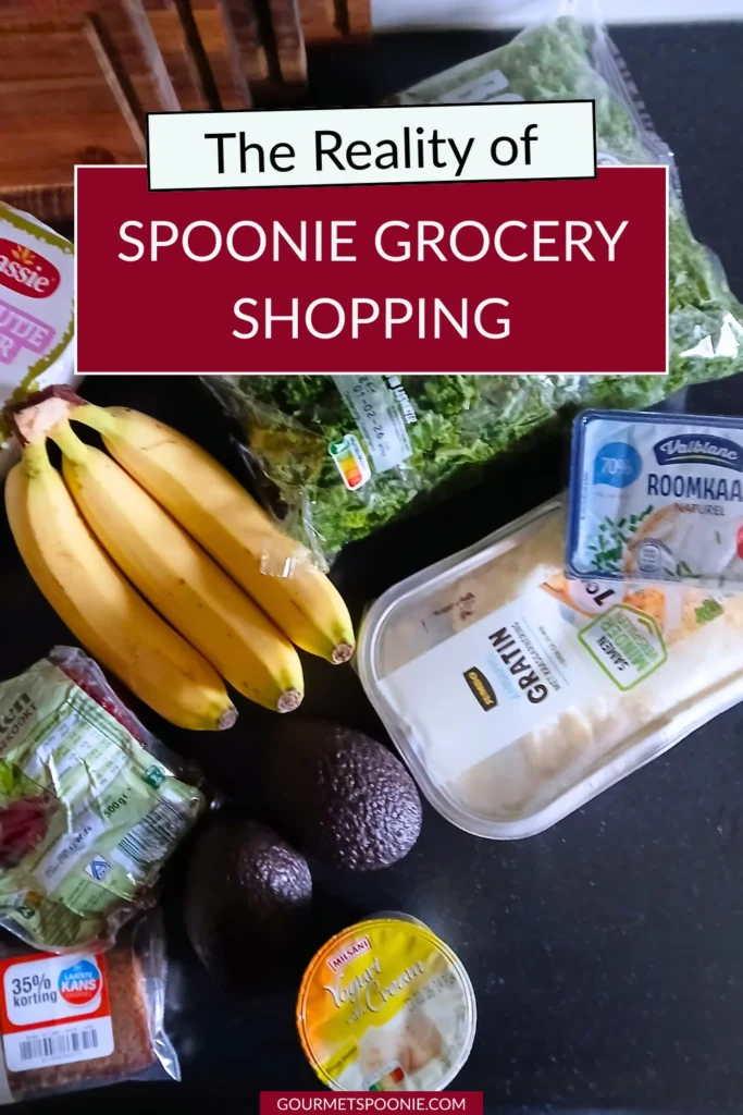 A variety of groceries, including bananas, lettuce, avocados, cheese, bread, and canned soup, are arranged on a dark countertop. Text overlay reads, The Reality of Spoonie Grocery Shopping.