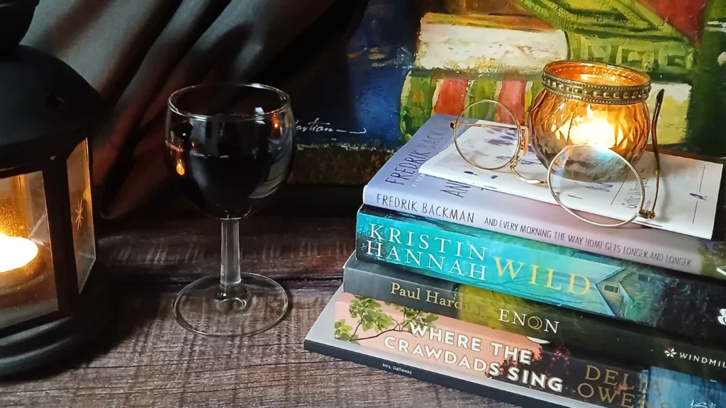 Cosy reading scene with stacked novels, candlelight, a glass of red wine, and glasses — evoking an accessible home library design in warm autumn tones.