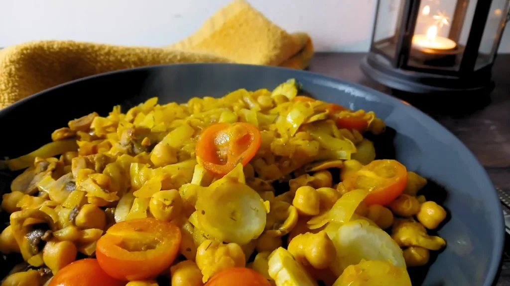 A close-up of a black plate filled with a chickpea and vegetable curry, topped with sliced cherry tomatoes. An easy Spoonie Meal Hack for hard days.