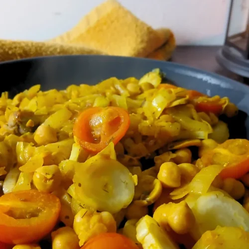 A close-up of a black plate filled with a chickpea and vegetable curry, topped with sliced cherry tomatoes. An easy Spoonie Meal Hack for hard days.