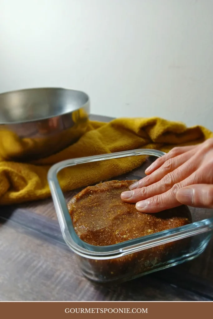 Thick chocolate date mixture being pressed into a container for no-bake energy bites.
