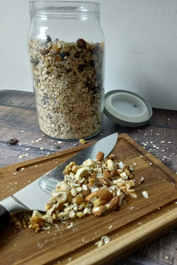 Glass jar of easy gluten-free muesli and a chopping board with knife and chopped nuts.