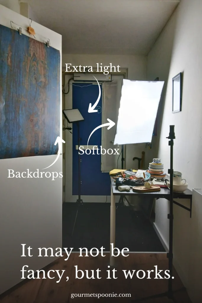 A small home studio set-up with a softbox light, an extra light, a blue backdrop, and a table with dishes and teacups. Text reads: It may not be fancy, but it works.