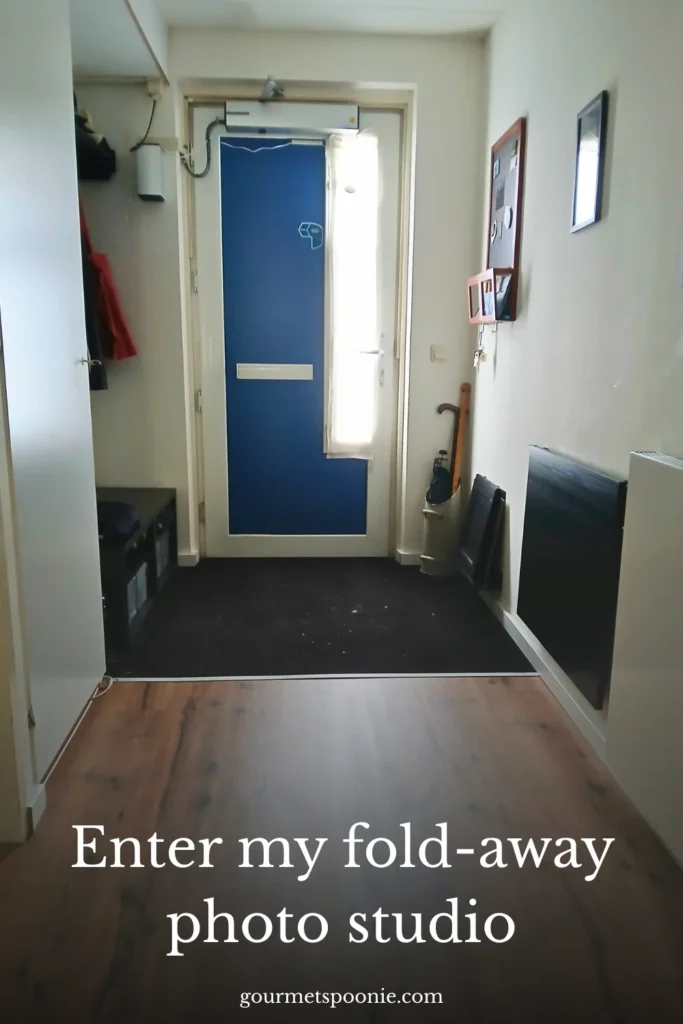 A small entrance hall with a blue front door, natural light coming from a tall window, benches along the walls, and the text Enter my foldaway photo studio at the bottom.