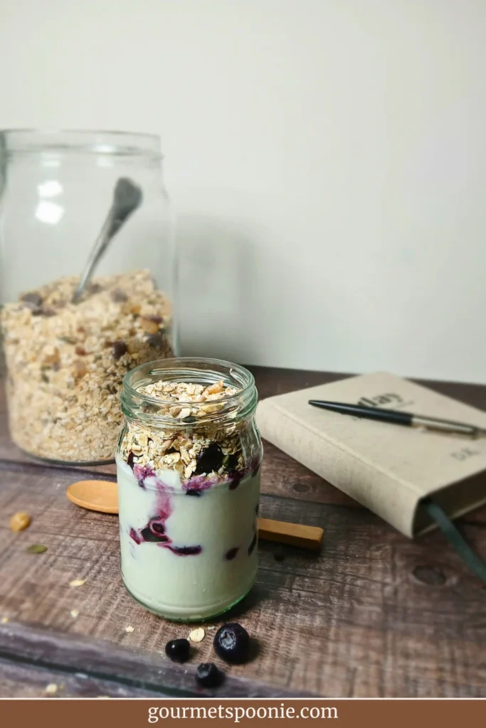 Single yoghurt parfait jar with muesli and berries on a rustic surface, styled as a simple low-energy breakfast option.