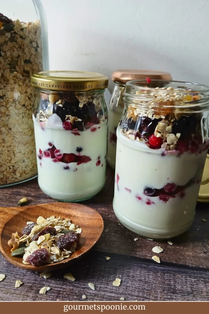 Muesli and yoghurt parfait in glass jars with layers of yoghurt, berries, and gluten-free muesli, styled as a healthy make-ahead breakfast.
