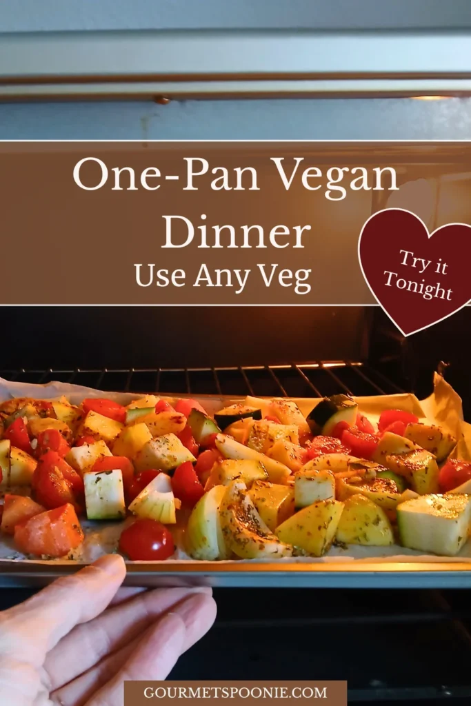 Hand placing a tray of seasoned mixed vegetables into the oven for a vegan roasted vegetable traybake