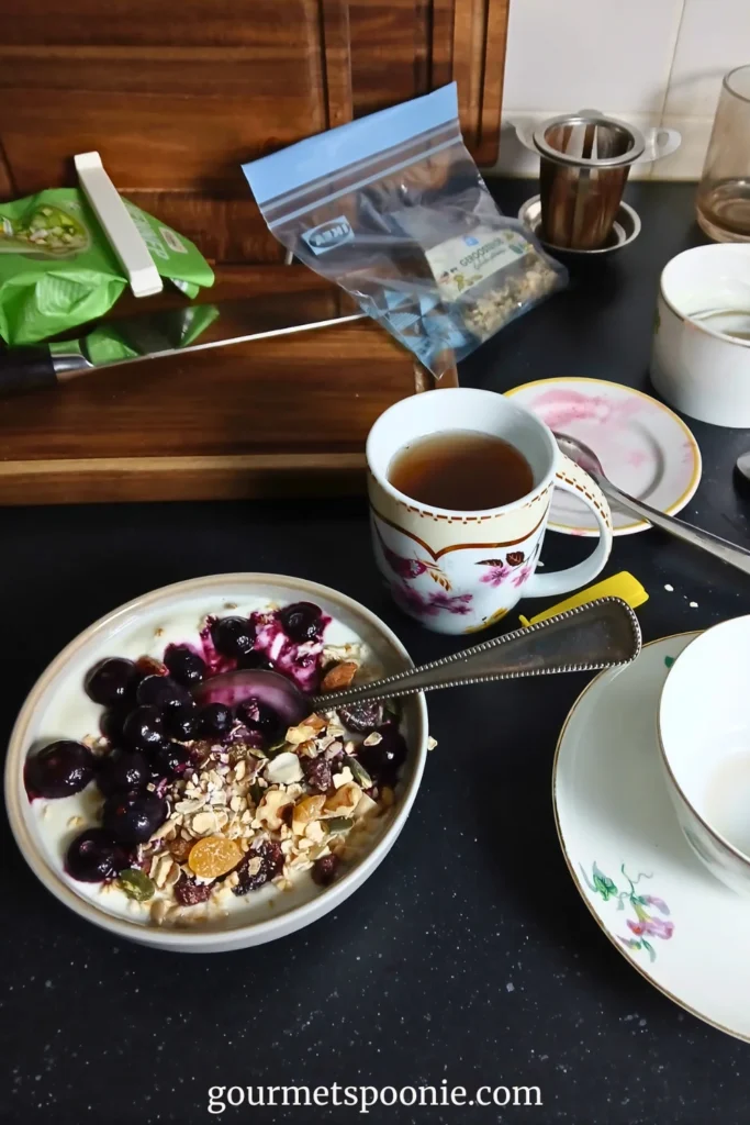 A bowl of yoghurt with muesli and berries and a cup of tea on a messy worktop after a recipe photoshoot