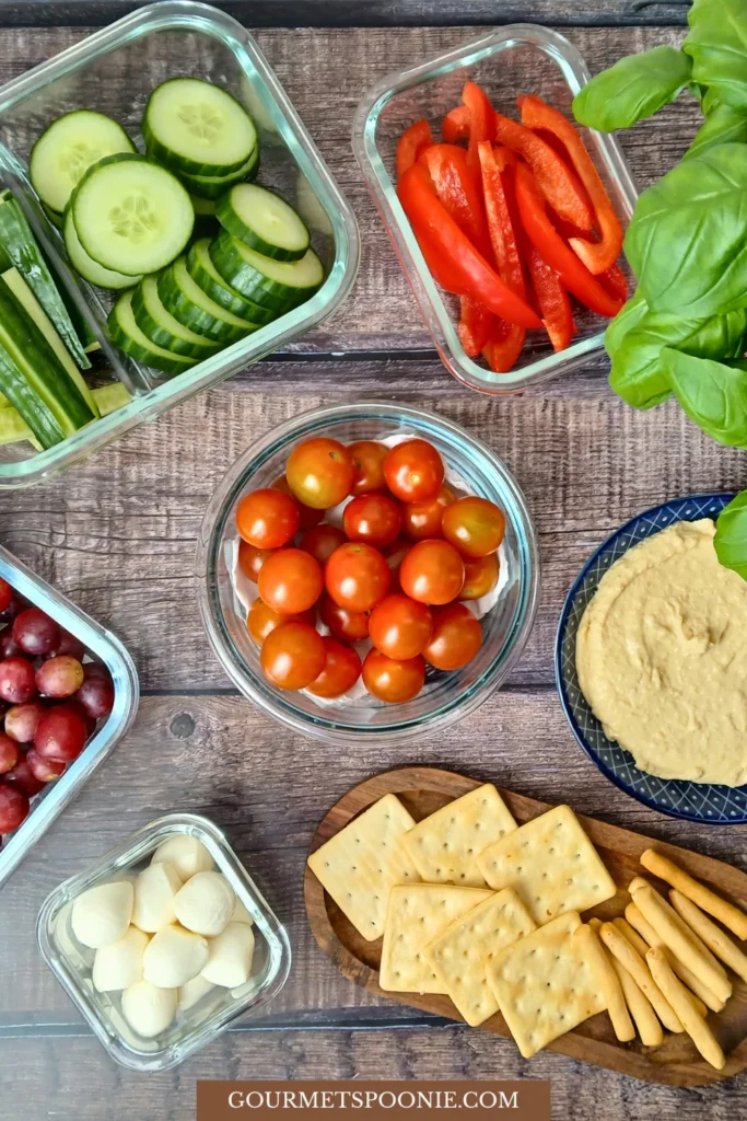 Ingredients for DIY lunchables including vegetables, gluten-free crackers, hummus, and fruit arranged on a table.