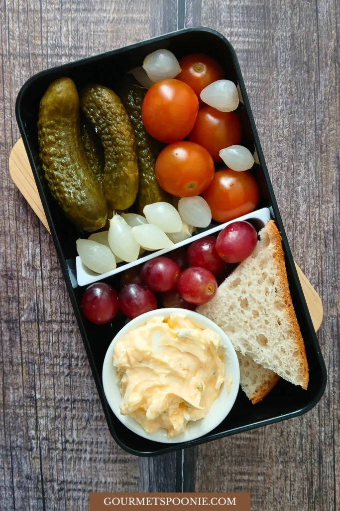Dutch-Inspired Lunchbox with gherkins, cherry tomatoes, silverskin onions, gluten-free bread, and egg salad.