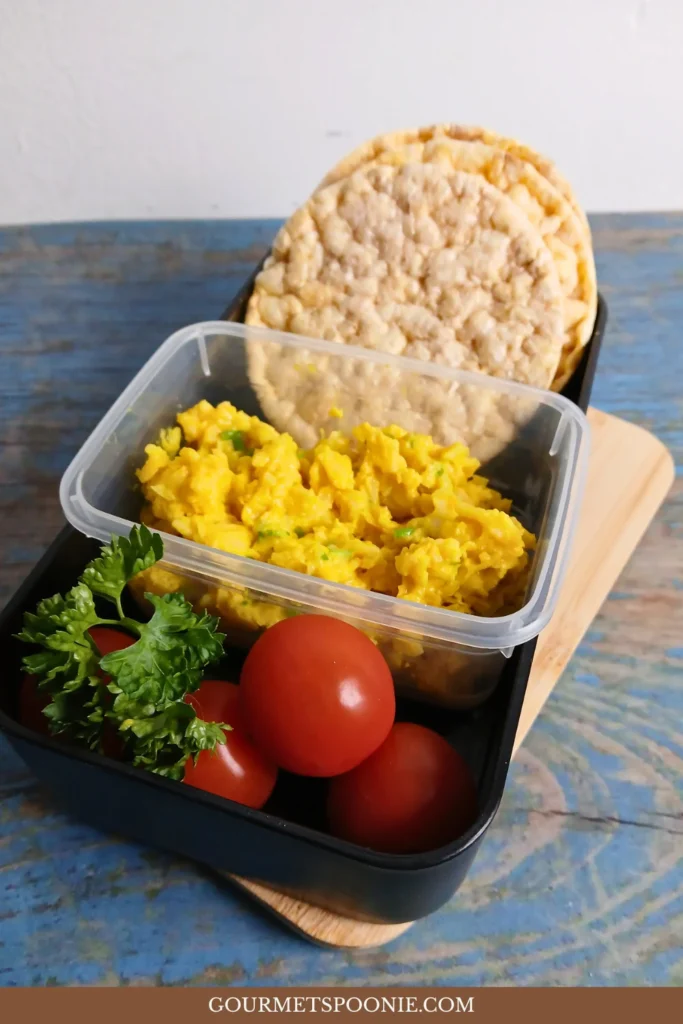 Lunchbox with high-protein vegan egg salad, corn thins, and cherry tomatoes.