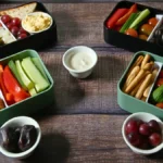 Four healthy lunchbox ideas with different ingredients, including vegetables, hummus, bread sticks, and fruit.