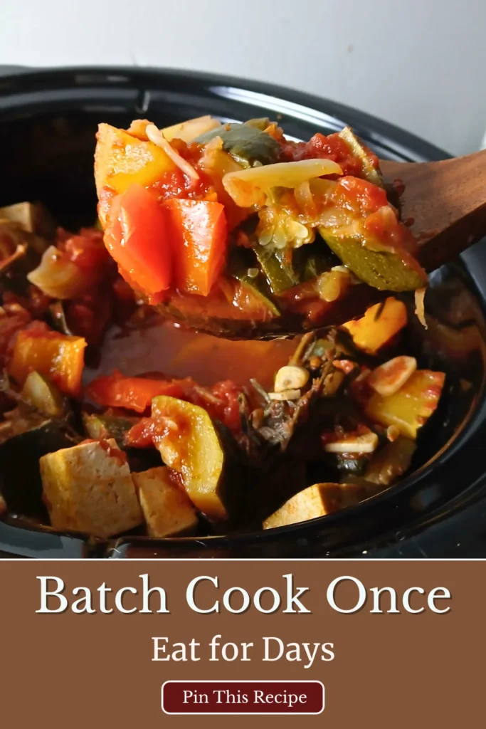 Wooden spoon lifting thick vegetable ratatouille from a slow cooker.