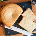 Flat lay of round, sliced lentil bread on cutting board, with knife and cup of tea.