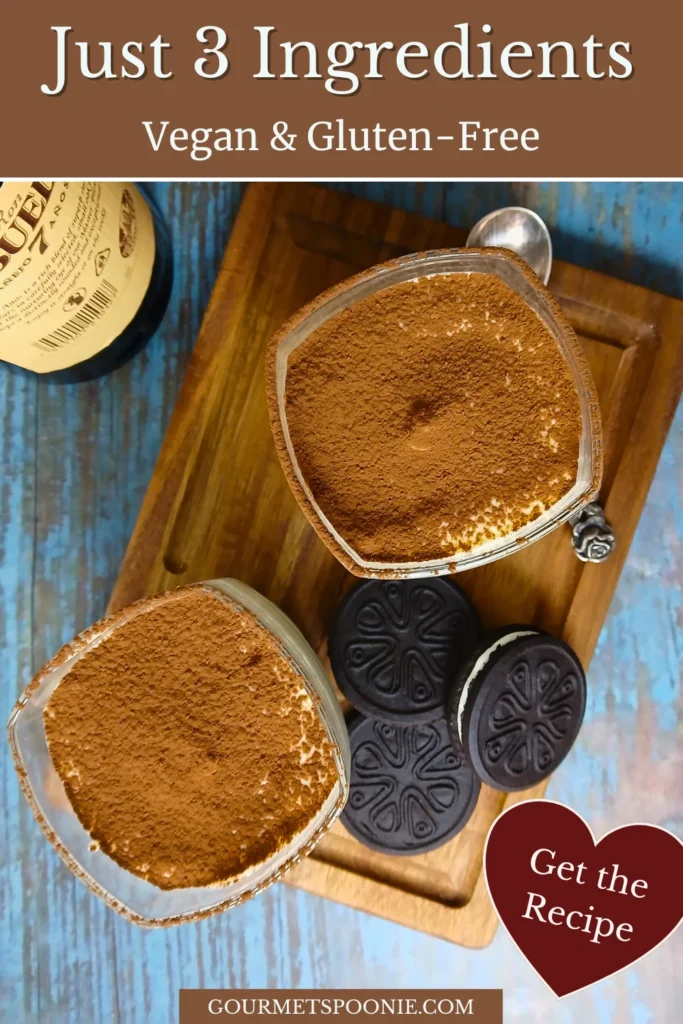 Overhead view of two vegan tiramisu-style cheesecake cups dusted with cocoa powder on a wooden board with gluten-free sandwich biscuits.