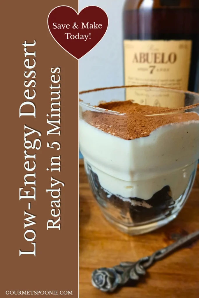 A single vegan tiramisu-style cheesecake cup topped with cocoa powder, photographed beside gluten-free biscuits and a bottle of rum on a wooden serving board.