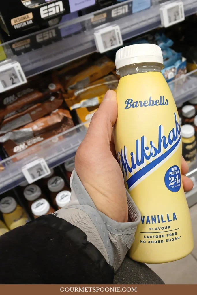 Hand holding a bottled protein shake in a supermarket aisle.