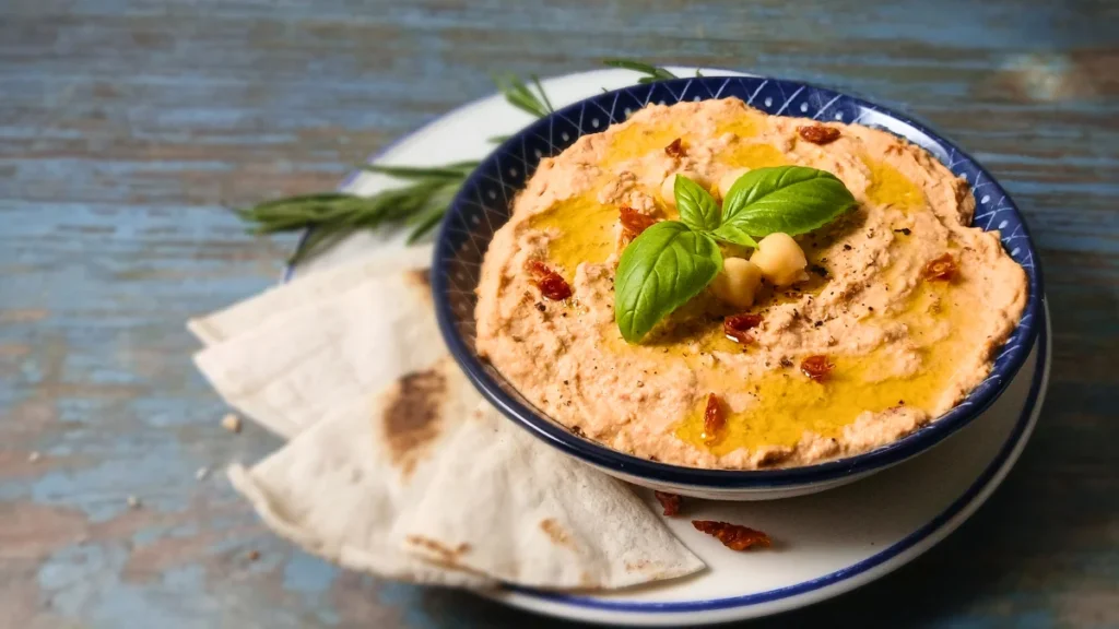 Creamy homemade sun-dried tomato hummus garnished with basil and olive oil, served with warm pita bread.
