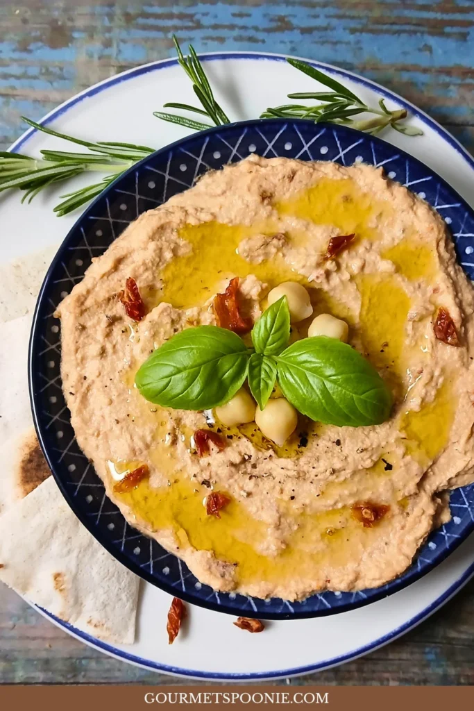 Creamy homemade sun-dried tomato hummus garnished with basil and olive oil in a blue bowl.