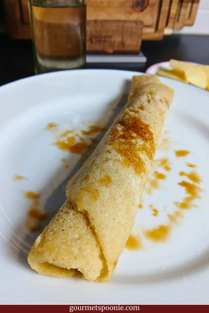 A rolled Dutch pancake on a white plate with syrup drizzled over the top. One of 10+ gluten-free vegan breakfast ideas for Spoonies.