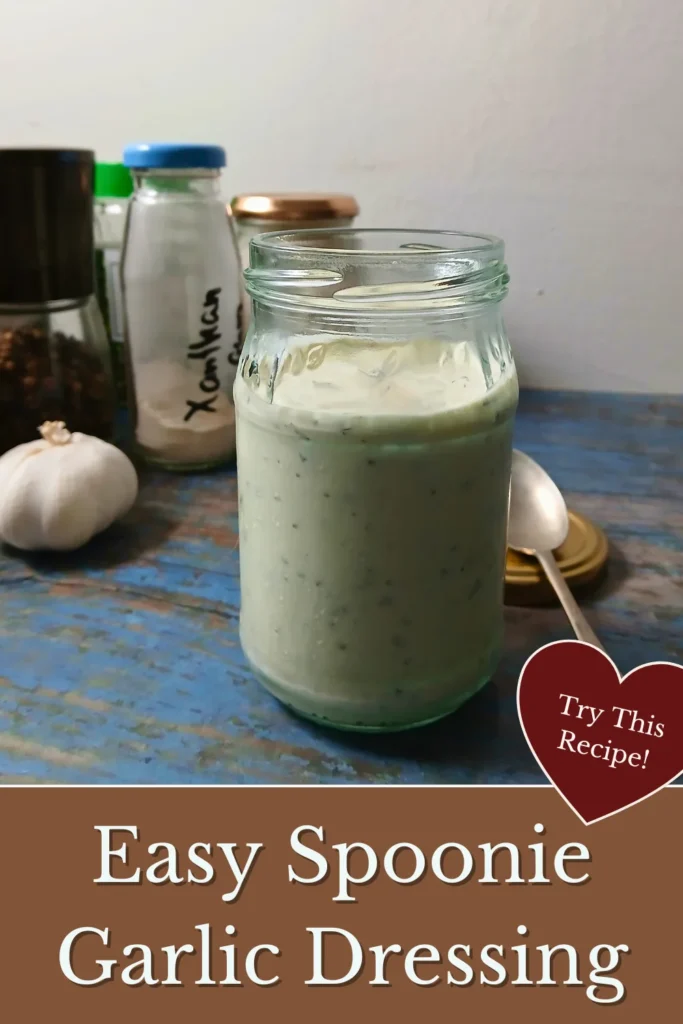 Glass jar filled with thick garlic yoghurt dressing on a rustic blue surface with garlic and herbs.