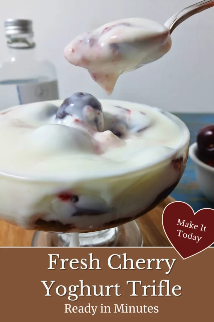 Spoon lifting creamy yoghurt and cherries from a homemade cherry yoghurt trifle in a glass serving bowl.