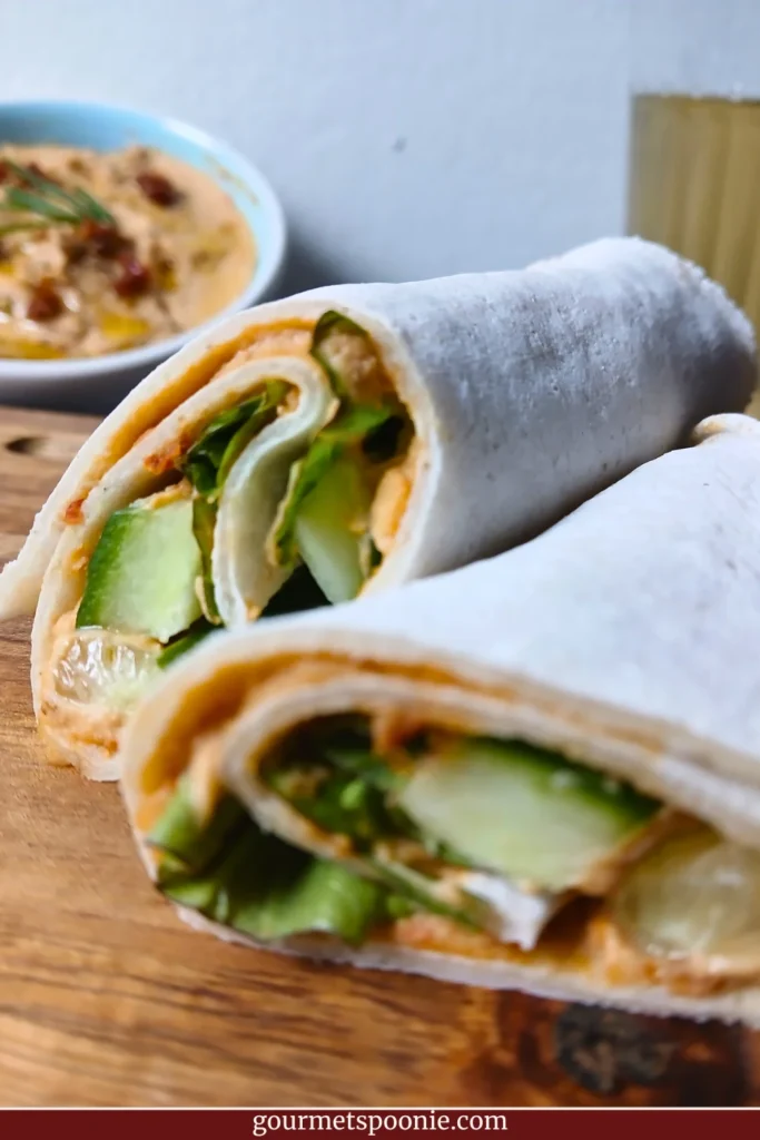 A gluten-free wrap filled with hummus, cucumber, and leafy greens, cut in half on a wooden board. One of several grab-and-go vegan breakfasts for Spoonies. 