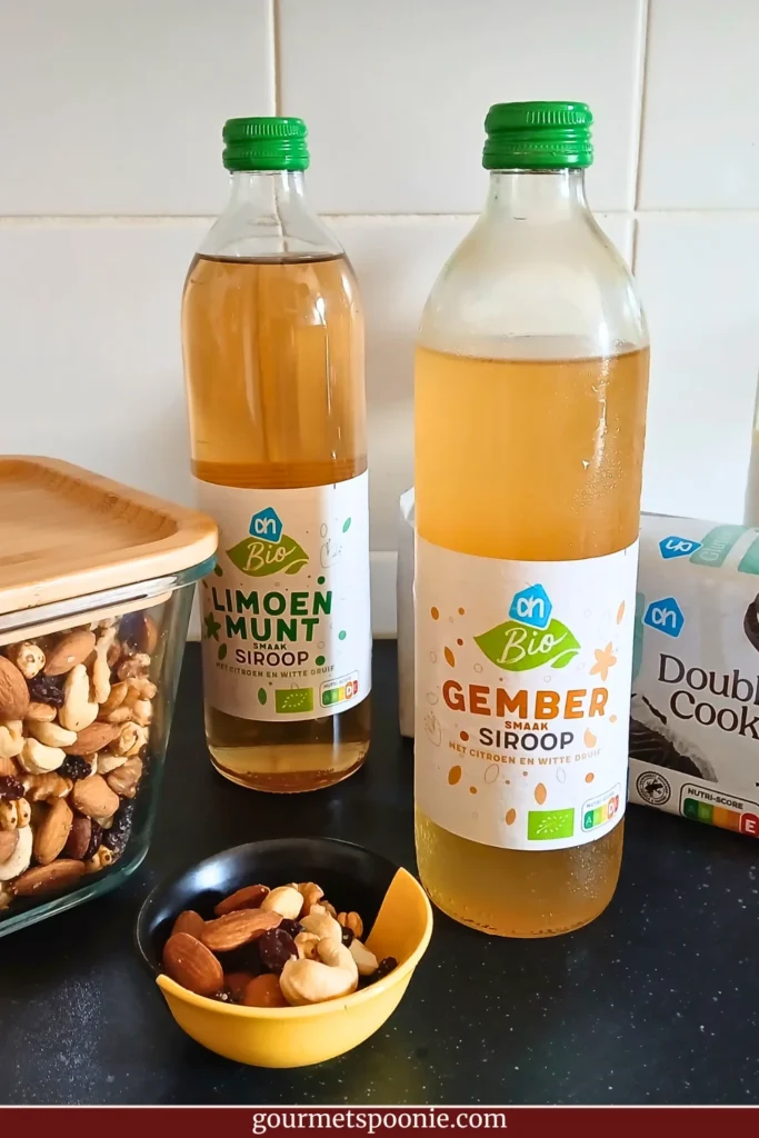 Two bottles of fruit squash, a bowl of trail mix, and gluten-free chocolate biscuits, arranged on a kitchen counter as part of a heatwave preparation with chronic illness plan.