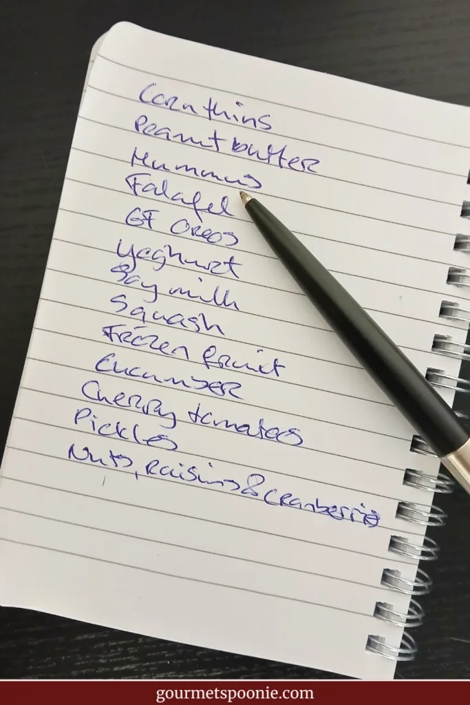 A handwritten shopping list beside a black pen on a notebook, photographed on a dark tabletop, representing planning and shopping for an upcoming heatwave.