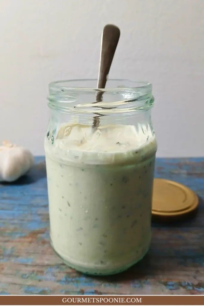 Creamy garlic yoghurt sauce in a glass jar with visible herbs