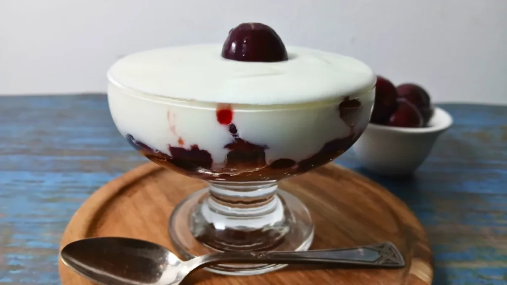 Single-serving cherry yoghurt trifle layered with leftover cake, cherry jam, fresh cherries, and creamy yoghurt in a glass dessert bowl, topped with a whole cherry.